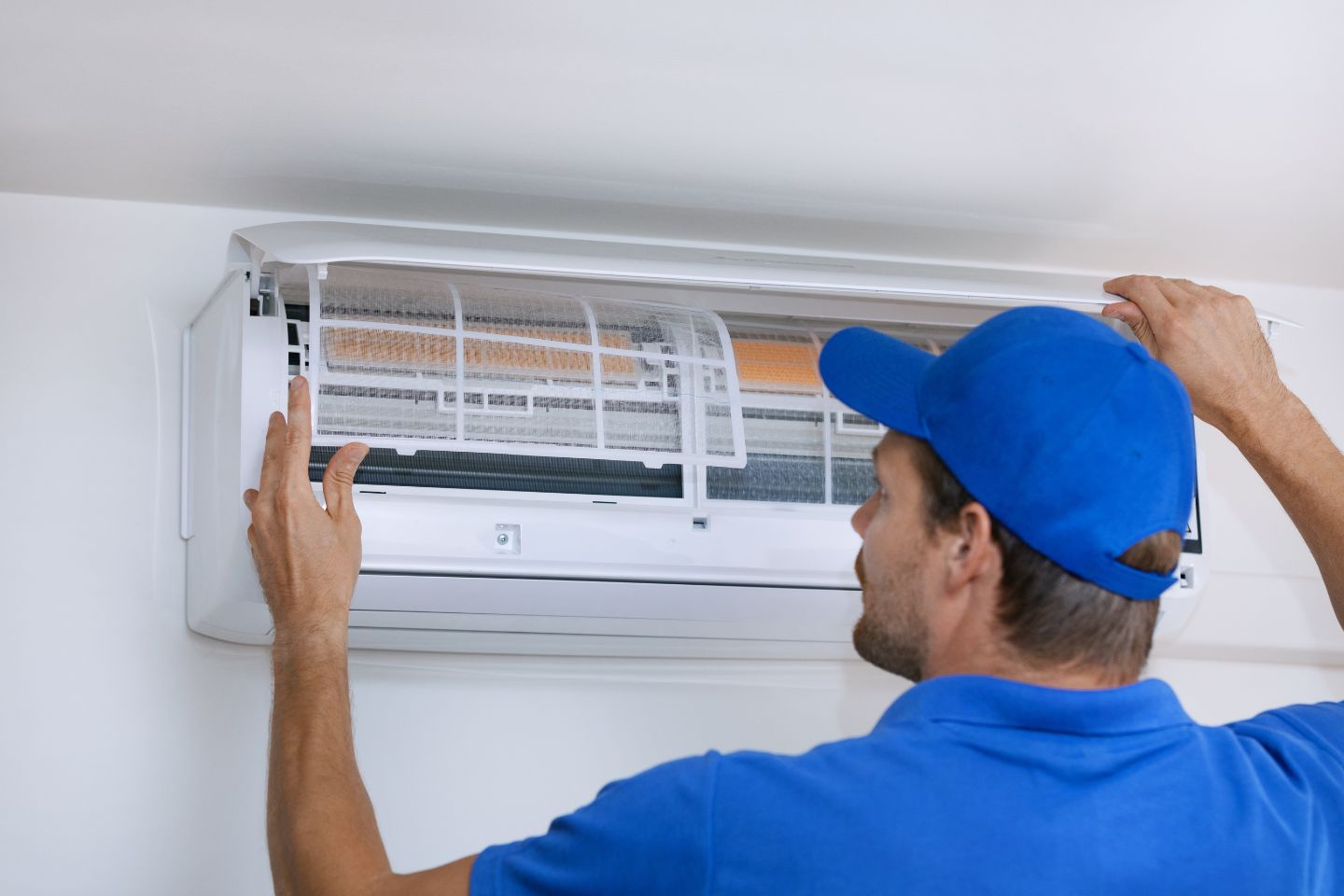 A man wearing a blue shirt and cap is fixing an air conditioner, showcasing HVAC mold removal services in Irvine, CA.
