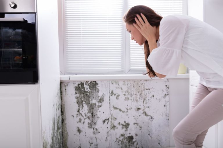A woman stands before a moldy wall, highlighting the health risks of inhaling mold spores, including cancer.